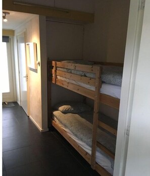 Een stapelbed in een kamer met een deur en een lamp aan de muur.