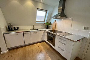 Une cuisine moderne avec des meubles blancs, une hotte en acier inoxydable, une fenêtre et un plancher en bois.