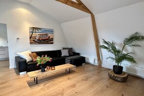 A modern living room with a black sofa, a wooden coffee table, a potted plant, and a painting of a vintage car on the wall. - Achter de Duinen||Castricum (Castricum)