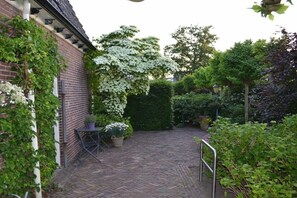 Un bâtiment en briques doté d’une cour pavée, entouré de diverses plantes et d’arbres.