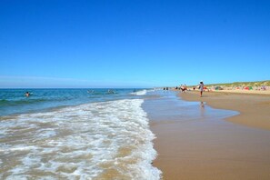 Une plage avec des vagues, des gens et des parasols.