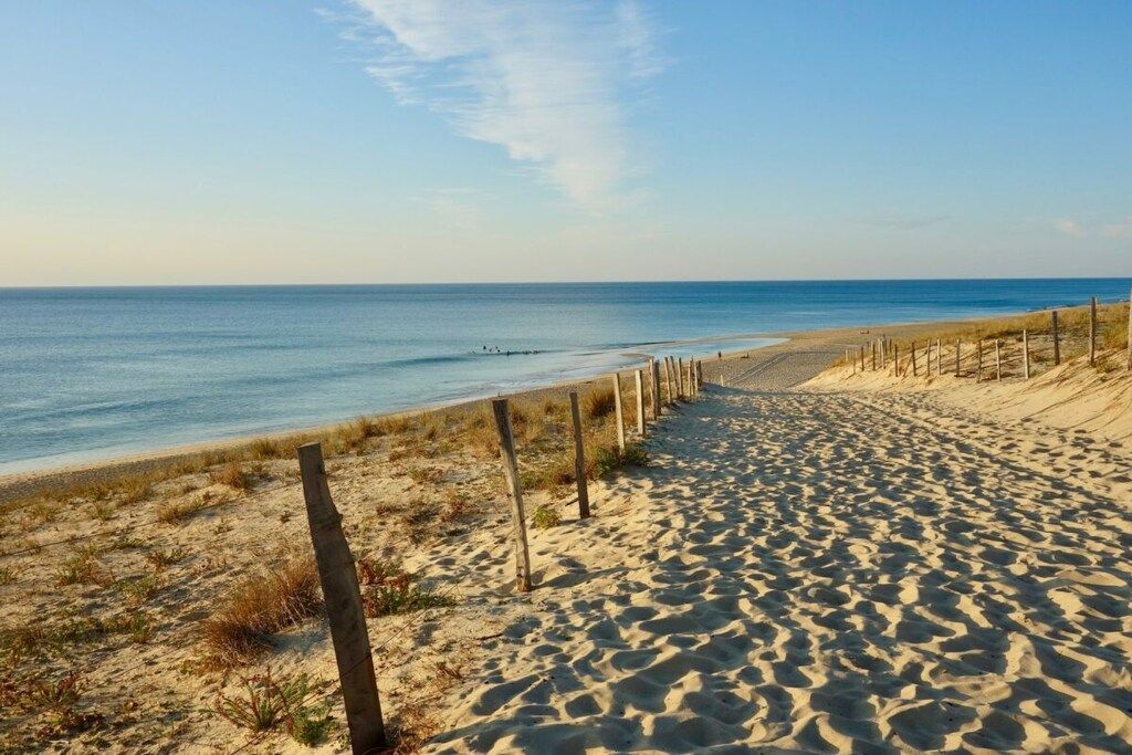 Ein Sandstrand mit einer Holzlattenveranda und blauem Himmel.