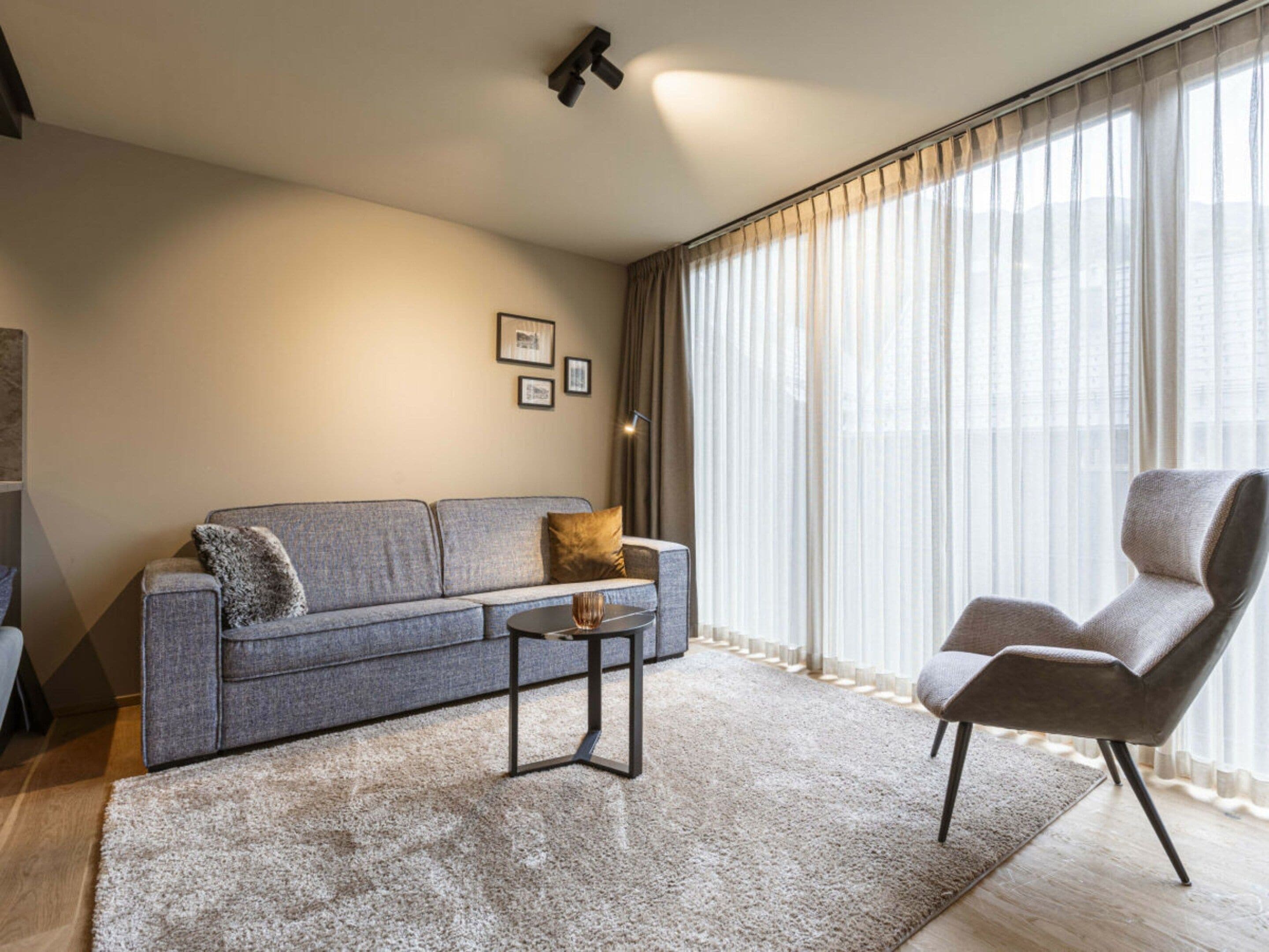 Un salon moderne avec un canapé gris, une petite table basse et un fauteuil en cuir.
