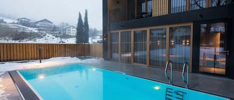 A swimming pool with a wooden deck and a view of a building with large windows and balconies.