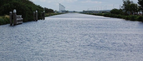 Un canal bordé d’une promenade en bois d’un côté et surmonté d’un pont métallique au loin.
