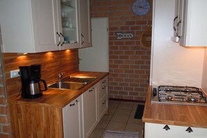 Eine Küche mit weißen Schränken, einer Kaffeemaschine, einem Spülbecken und einem Gaskochfeld.