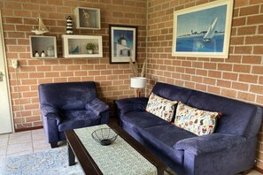 A living room with a brick wall, two sofas, a coffee table, and framed artwork. - in the Geestmerambacht bungalow park (Schoorldam)