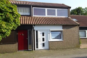 Ein zweistöckiges Wohngebäude mit roter Tür, kleinem Fenster und Ziegelaußenwand.