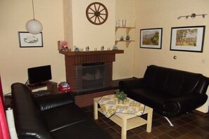 Ein Wohnzimmer mit Kamin, einer schwarzen Ledersofa, einem Holztisch und einem Fernseher auf einem Schrank.