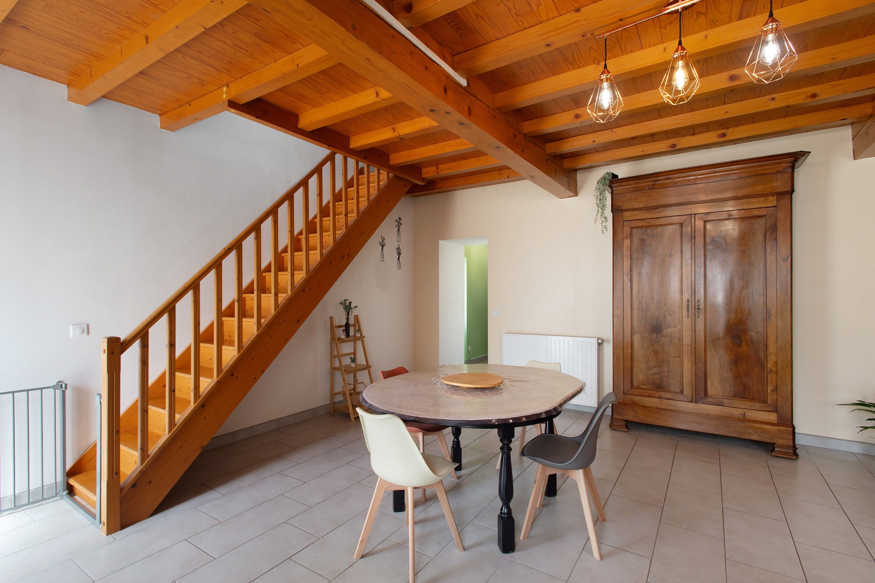 A dining area with a wooden staircase, a round table with chairs, and a large wooden cabinet.