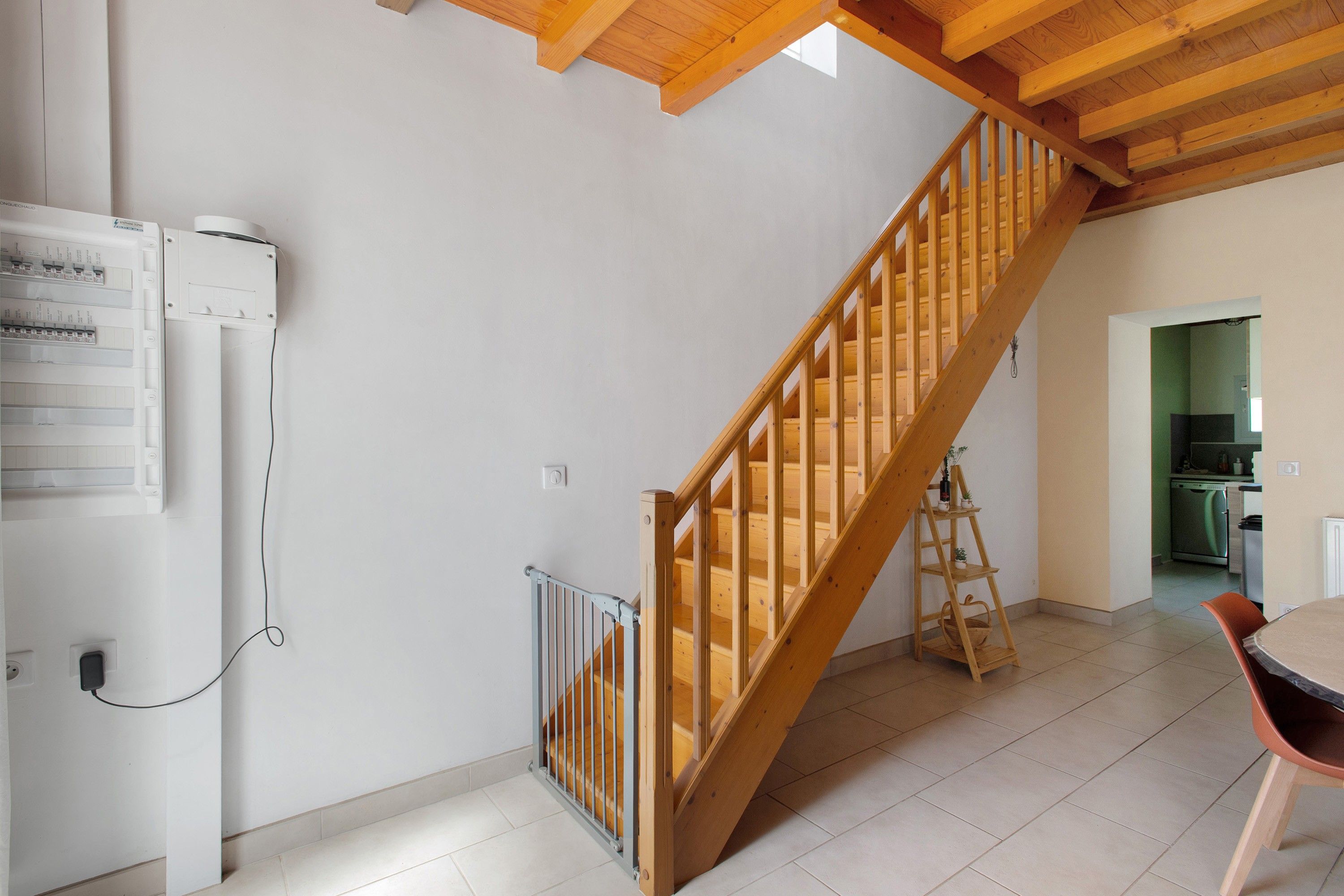 Un escalier avec des rampes en bois menant à l’étage supérieur, un coin cuisine équipé d’un lave-vaisselle et une table à manger avec des chaises.