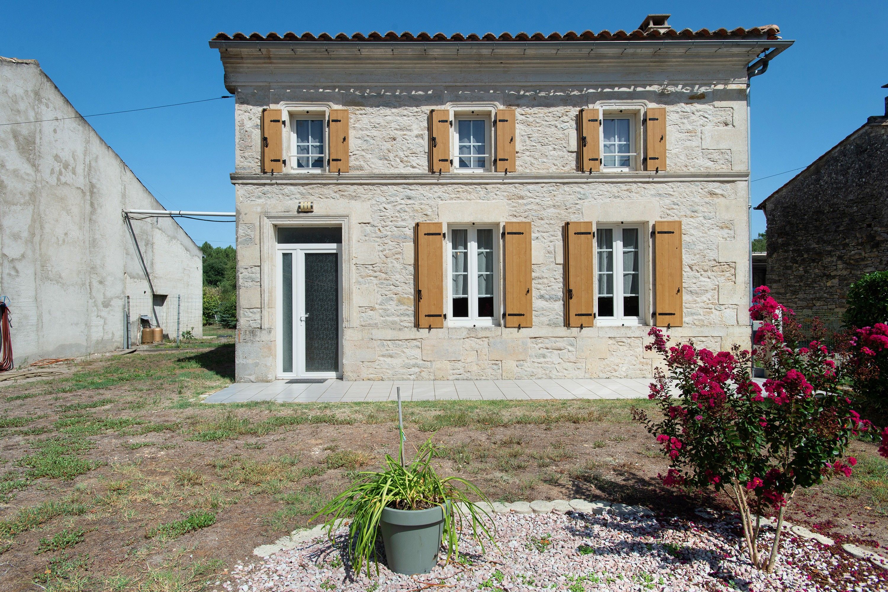 A two-story stone building with a tiled roof, a front door, and wooden shutters.