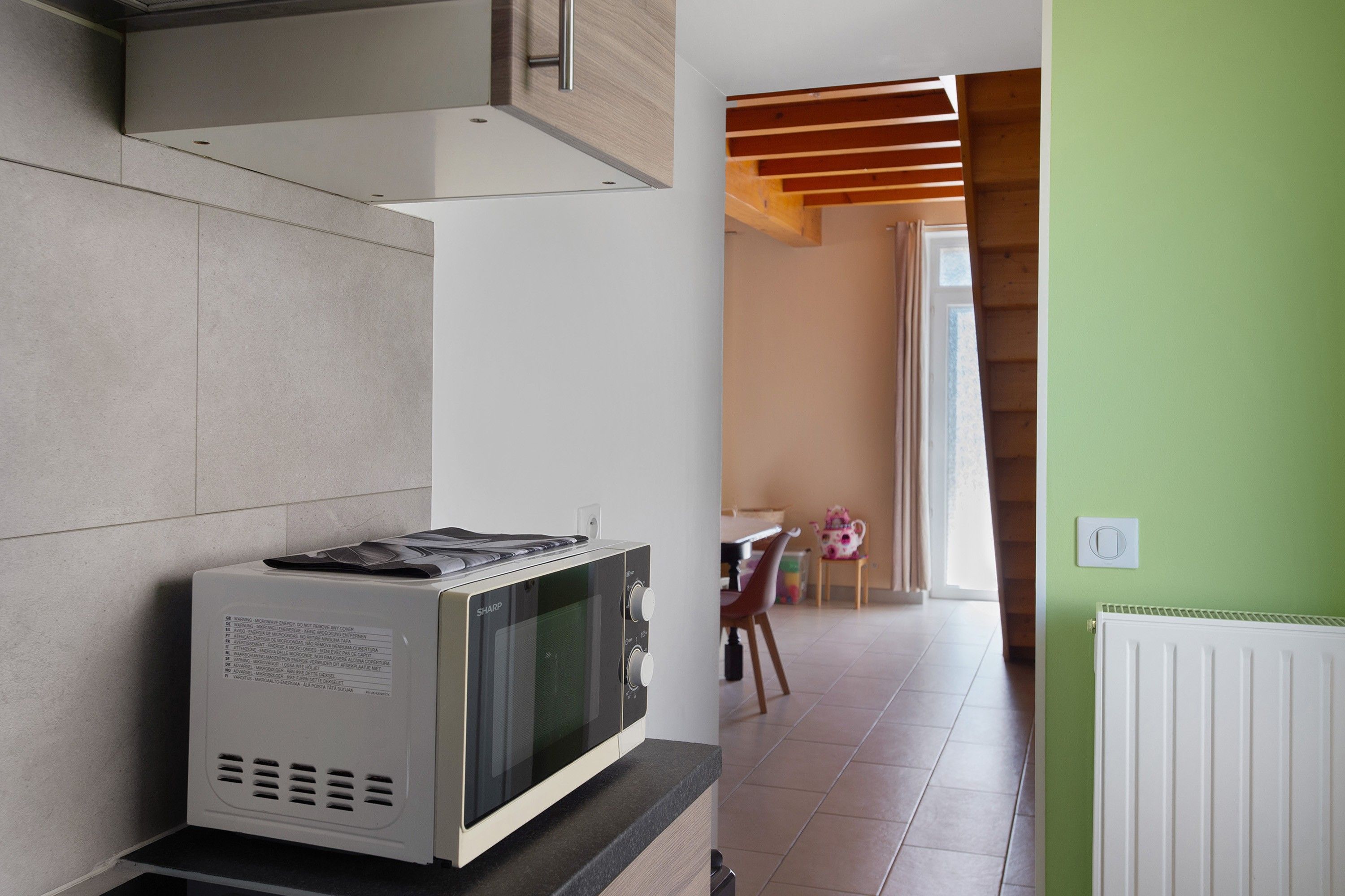 Una cucina con un forno a microonde sul bancone, una finestra e un'area pranzo con una sedia e un tavolo.