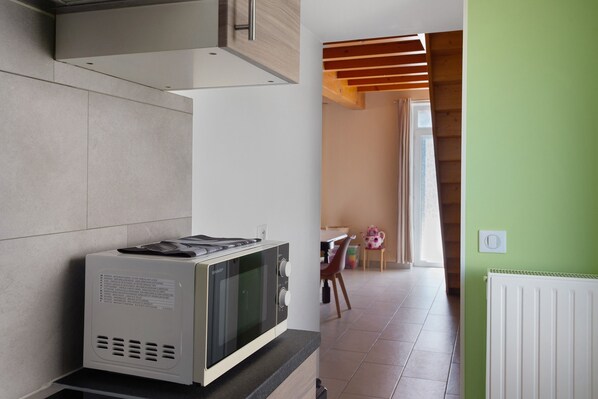 Una cucina con un forno a microonde sul bancone, una finestra e un'area pranzo con una sedia e un tavolo.