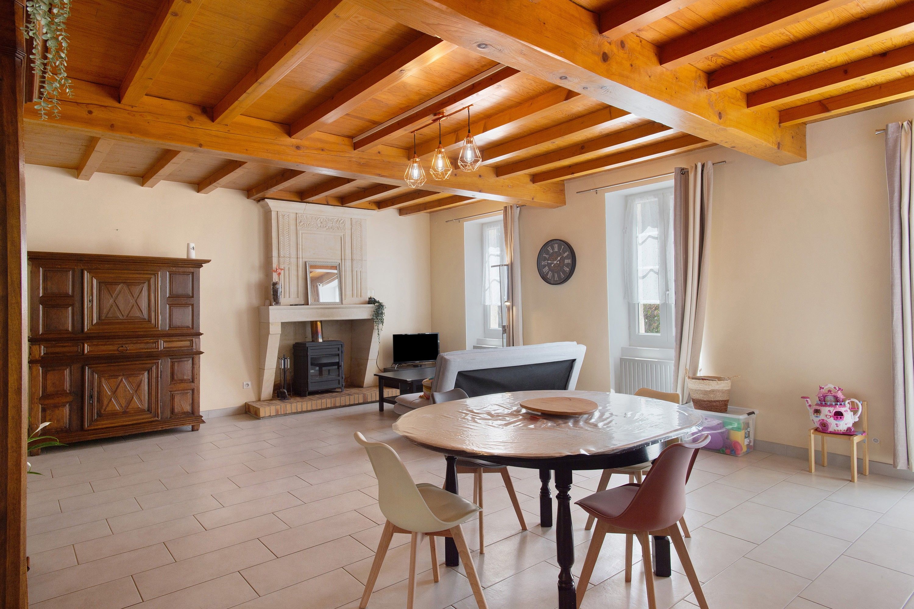 Un'ampia stanza con soffitto in legno a vista, un camino, un tavolo da pranzo con sedie e una televisione.