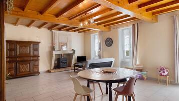 Un'ampia stanza con soffitto in legno a vista, un camino, un tavolo da pranzo con sedie e una televisione.
