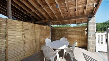 Una terrazza esterna con tavolo e sedie di legno, una recinzione in legno e un muro in pietra.