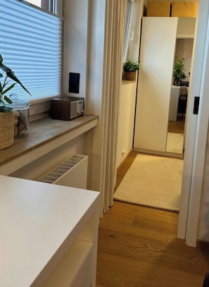 En smal hall med ett element, en krukväxt och ett vitt skåp.