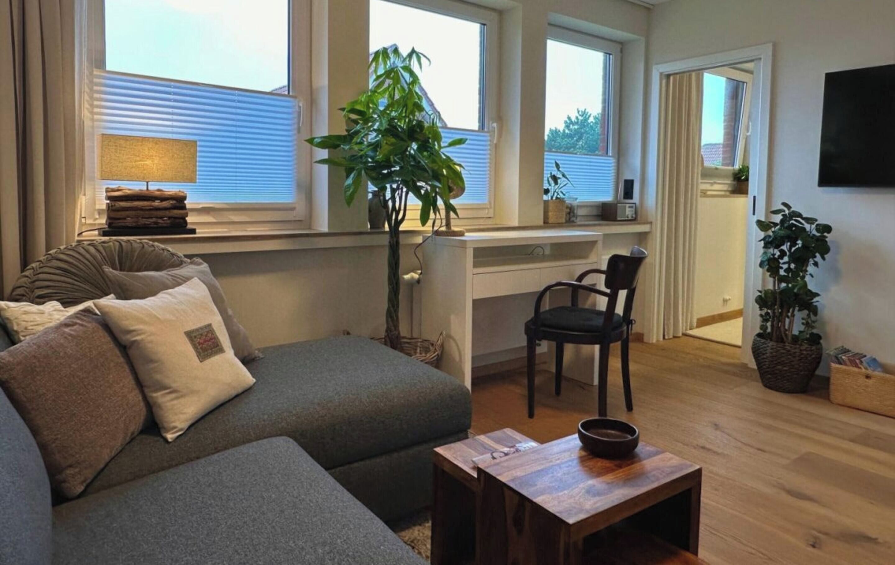Een moderne woonkamer met een bank, een klein tafeltje, een stoel en een werkplek met een plant.