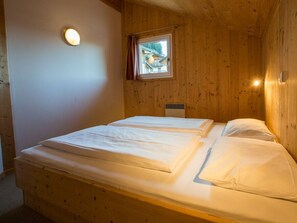 Quarto de cabana de madeira com duas camas, janela com cortinas e luminária na parede.