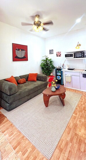 A living room with a sofa, a coffee table, a ceiling fan, and a kitchen area with a microwave. - Nary Home Private1BR near My Khe BeachI Sleeps 4 I Kitchen l Washer Dryer l 2 AC (Đà Nẵng)