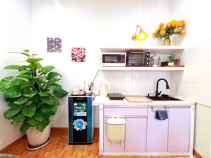 Cozinha compacta com micro-ondas, torradeira e pia. Há uma planta em vaso e um pequeno armário com uma chaleira.