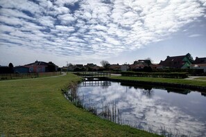 A serene residential area with a calm pond, a wooden bridge, and houses with distinct architectural styles. - Bungalow with 1 bedroom (Julianadorp aan Zee, Niederlande, Europa)