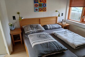 Ein Schlafzimmer mit einem hölzernen Kopfteil, zwei Einzelbetten, einem Nachttisch mit Lampe, einer kleinen Pflanze und einem farbenfrohen, abstrakten Gemälde an der Wand.