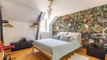 Een slaapkamer met een bed, een radiator, een raam, een hanglamp en een wand met tropische behang.