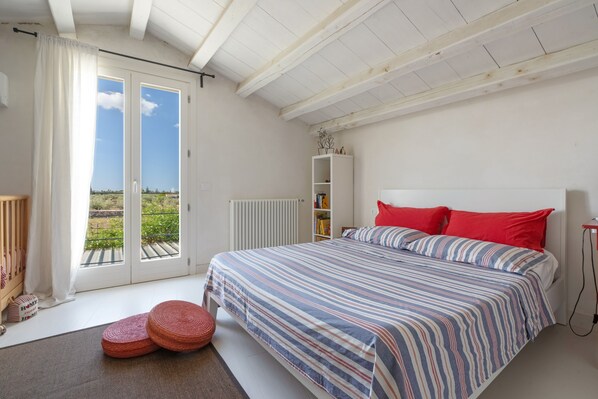 A bedroom with a bed, a radiator, a bookshelf, and a view of the outdoors.