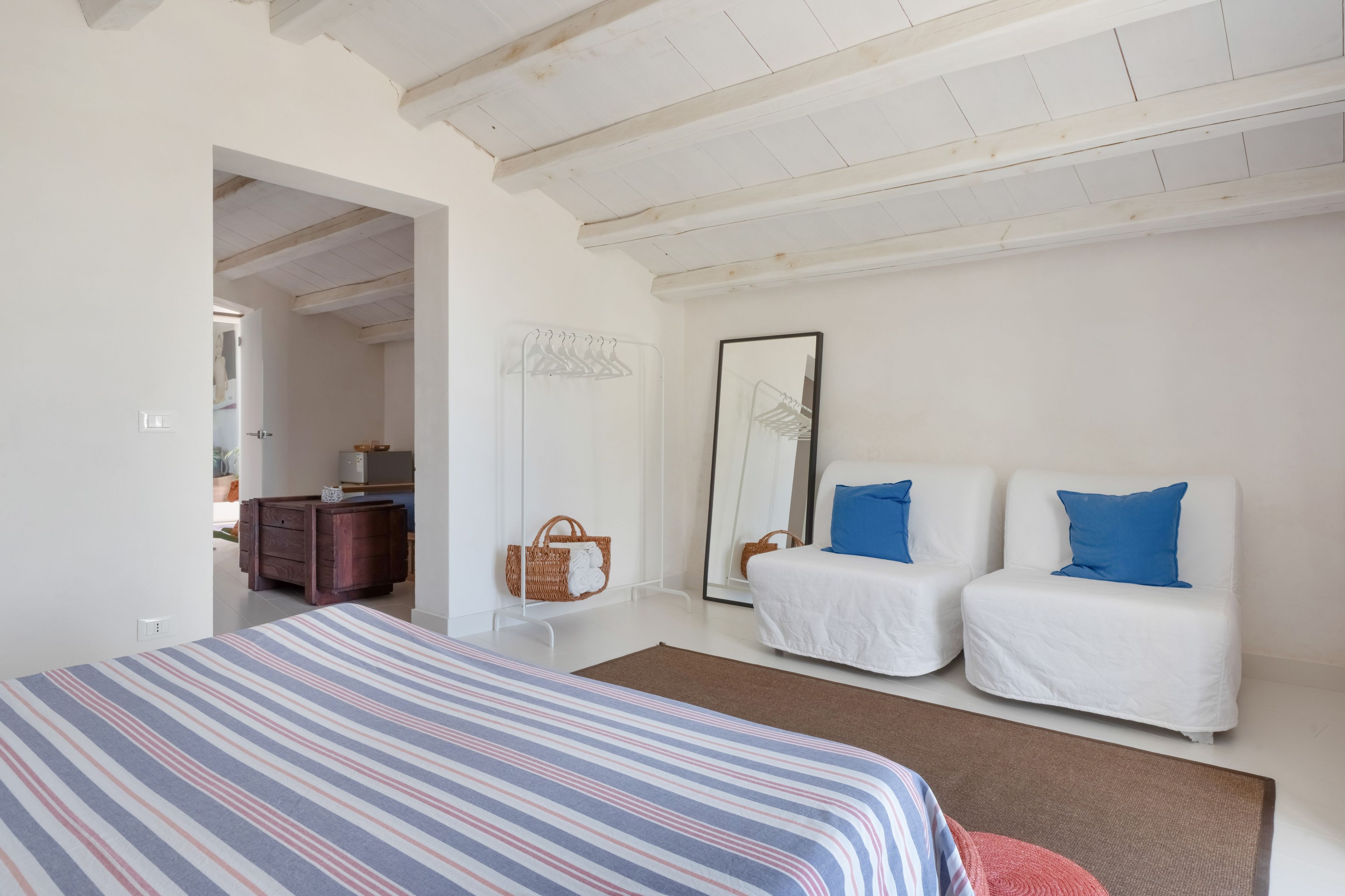 Ein Schlafzimmer mit einem großen Bett, zwei weißen Sofas mit blauen Kissen, einem hölzernen Schminktisch, einem hängenden Korb und einem Spiegel an der Wand.