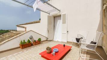 Une terrasse sur le toit avec une table rouge, deux chaises en osier blanches, des plantes en pot et un auvent blanc.
