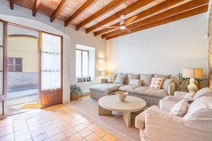 A cozy living room with a wooden ceiling, a large sofa set, a round coffee table, and a door leading outside. - Casa Barbarama - with private swimming pool (Alaro)