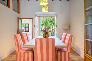 A dining area with a table and chairs, a vase with flowers, and a view of greenery outside. - Casa Barbarama - with private swimming pool (Alaro)