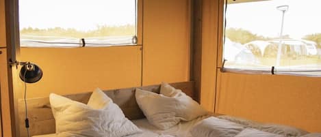 A double bed with a wooden headboard and two windows with curtains.