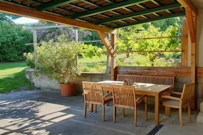 An outdoor wooden pergola with a table and chairs, surrounded by greenery and a garden. - 3 Weingut Hauerhof 99 (Klosterneuburg)
