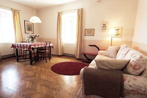 A cozy living room with a wooden herringbone floor, a red rug, a sofa, a dining table with chairs, and a lamp. - 3 Weingut Hauerhof 99 (Klosterneuburg)