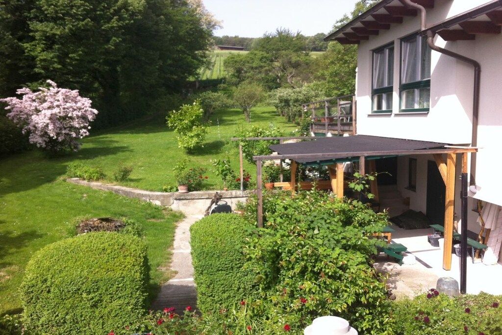 A house with a covered patio, a garden with various plants, and a clear view of the surrounding landscape.