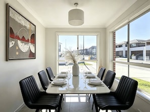 A dining area with a long table, black chairs, and a vase with dried plants. - JC House Park Side - 4 bedroom house (Bardia)