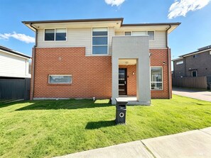 A two-story residential building with a brick facade, a front door, and a mailbox. - JC House Park Side - 4 bedroom house (Bardia)