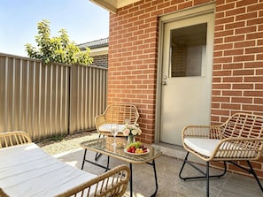An outdoor patio with wicker furniture, a glass table, and a door to a building. - JC House Park Side - 4 bedroom house (Bardia)