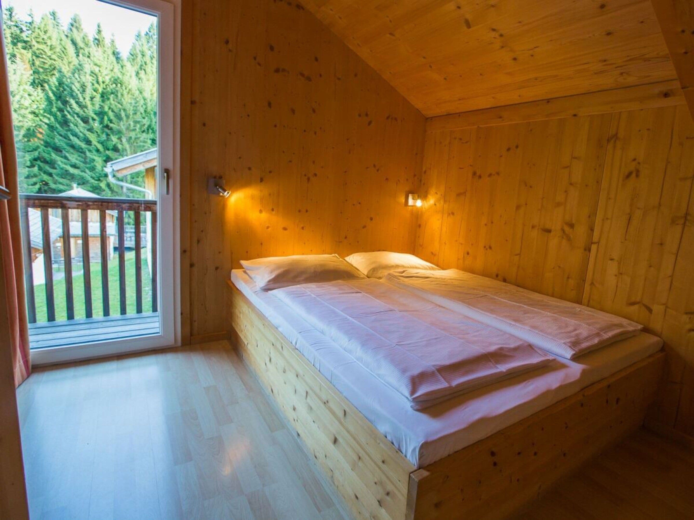 En stuga med träpanel, ett rum med en säng, ett fönster och en dörr som leder ut till en uteplats.