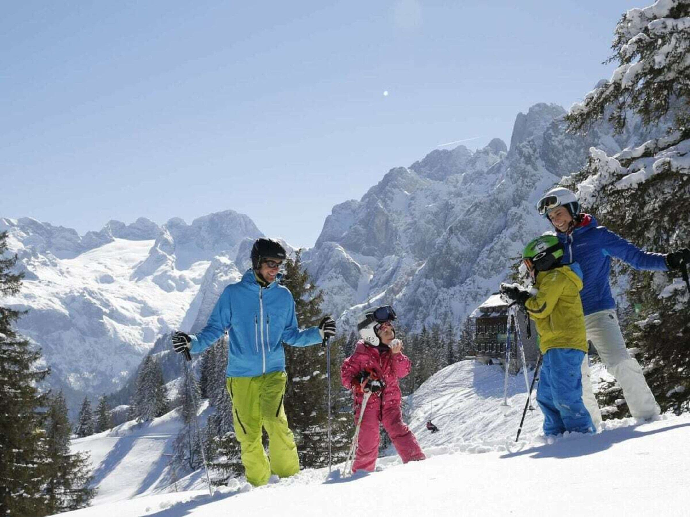 A group of people on a snowy mountain with ski equipment, surrounded by snow-covered trees and mountains.