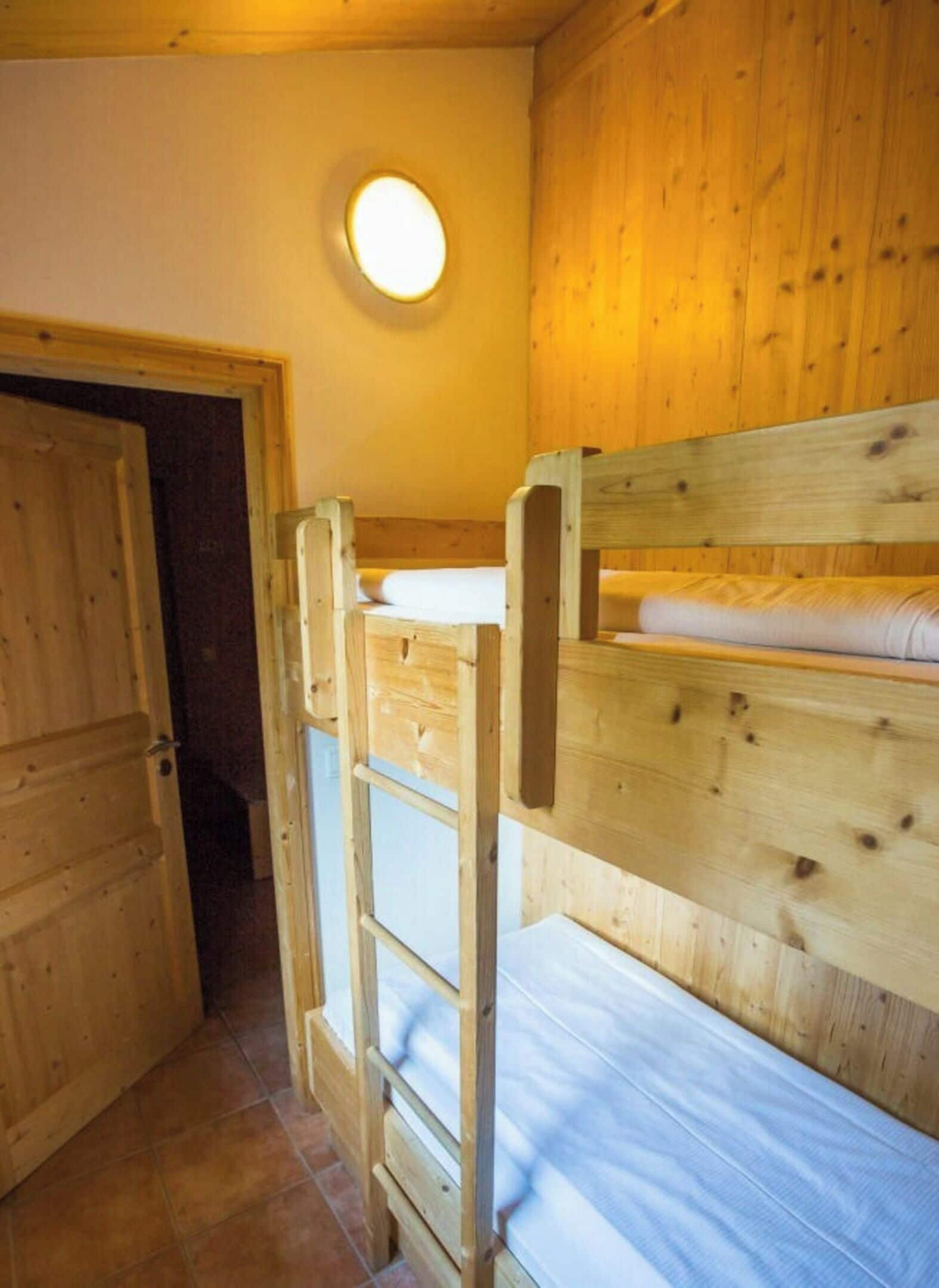 Et værelse med køjesenge i træ, en dør og en rund lampe på væggen.