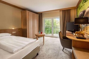 Ein Hotelzimmer mit Bett, Schreibtisch, Stuhl, Fernseher und einem Fenster mit Blick auf Grünflächen.
