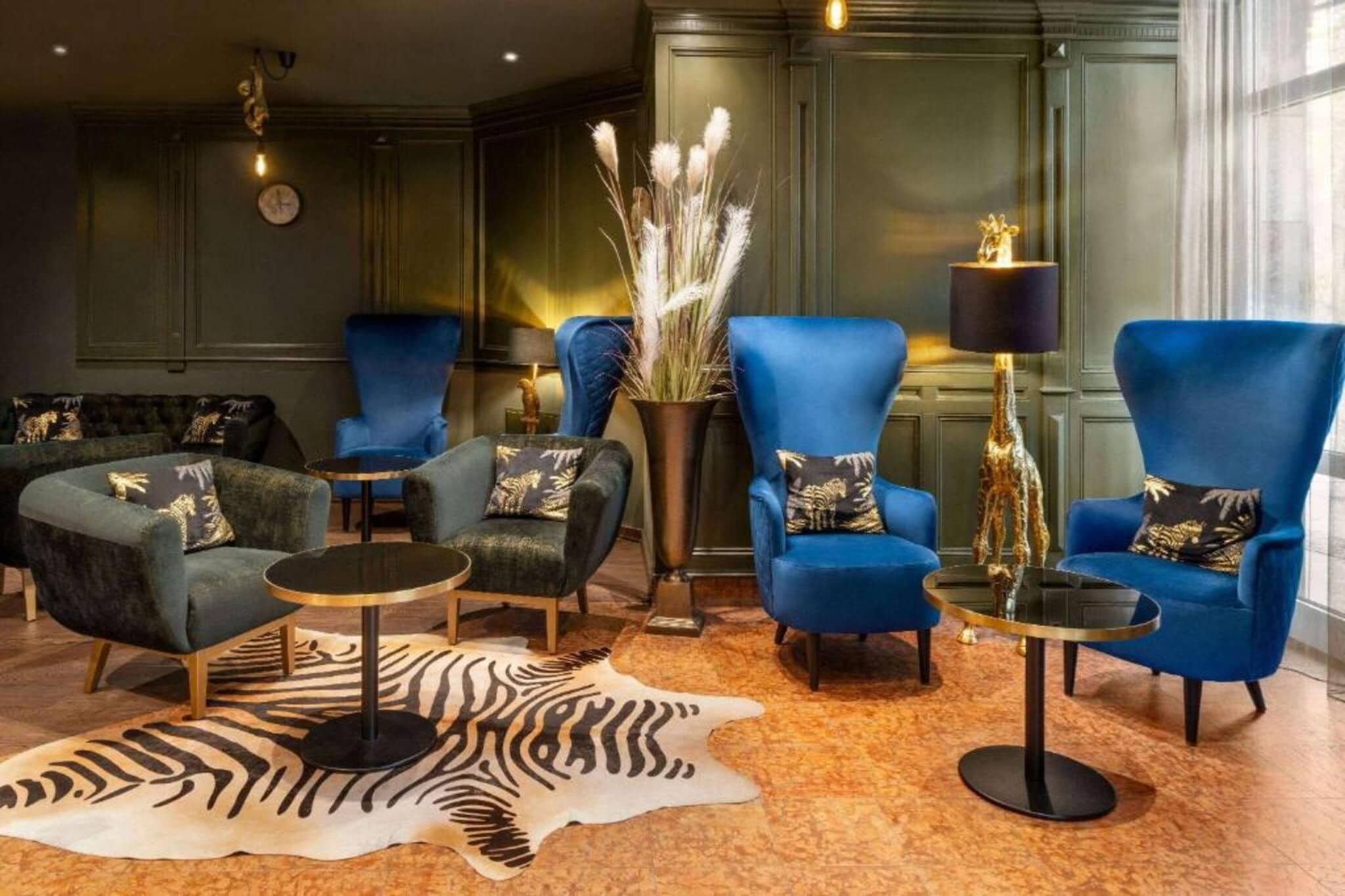A lounge area with blue armchairs, a zebra-patterned rug, and a vase with dried plants.
