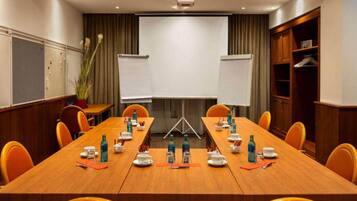 A conference room with a long table, chairs, whiteboards, and a projector screen.