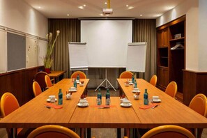 A conference room with a long table, chairs, whiteboards, and a projector screen.