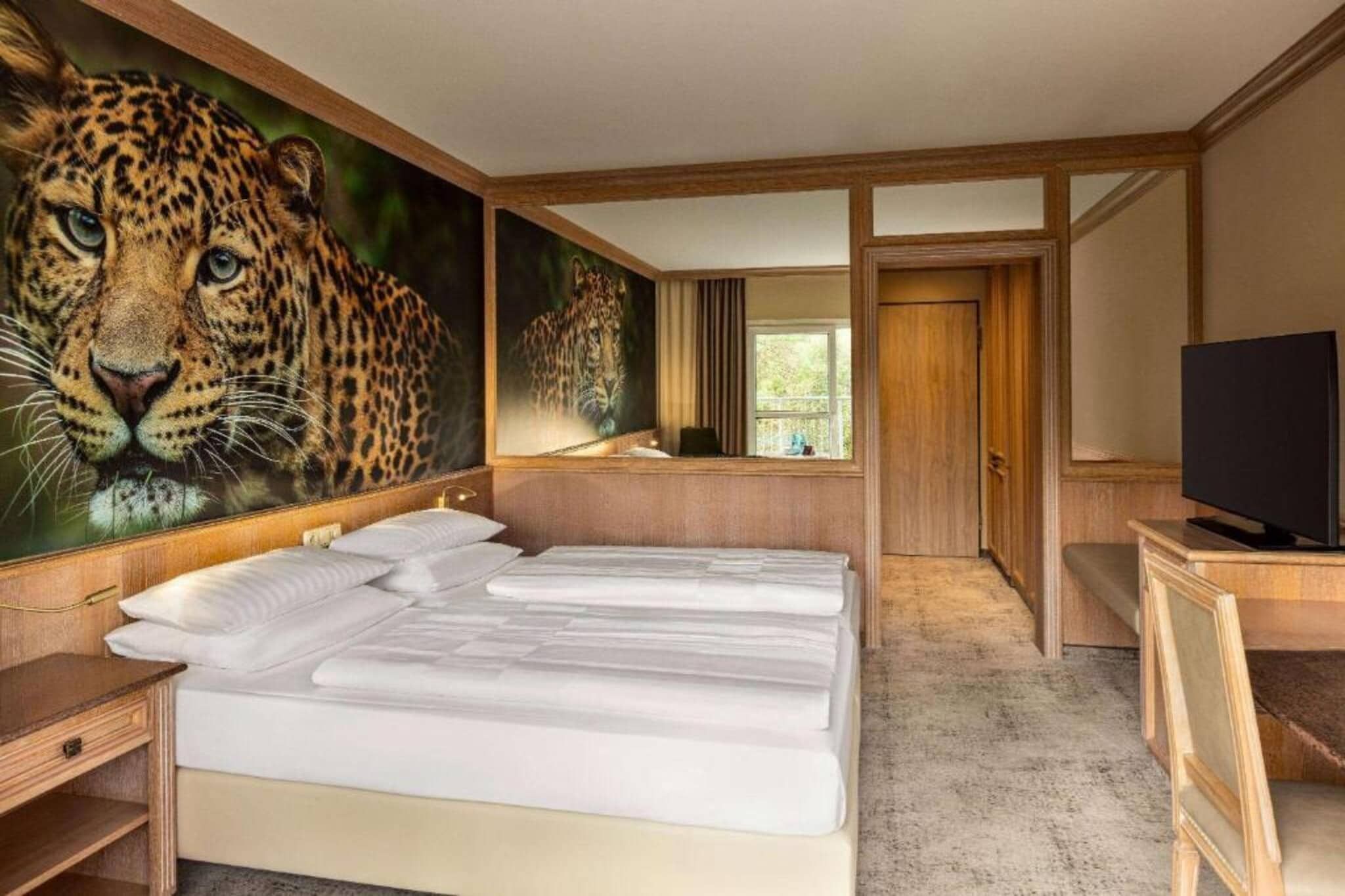 Une chambre d’hôtel avec un grand lit, une télévision et un tableau représentant un léopard accroché au mur.