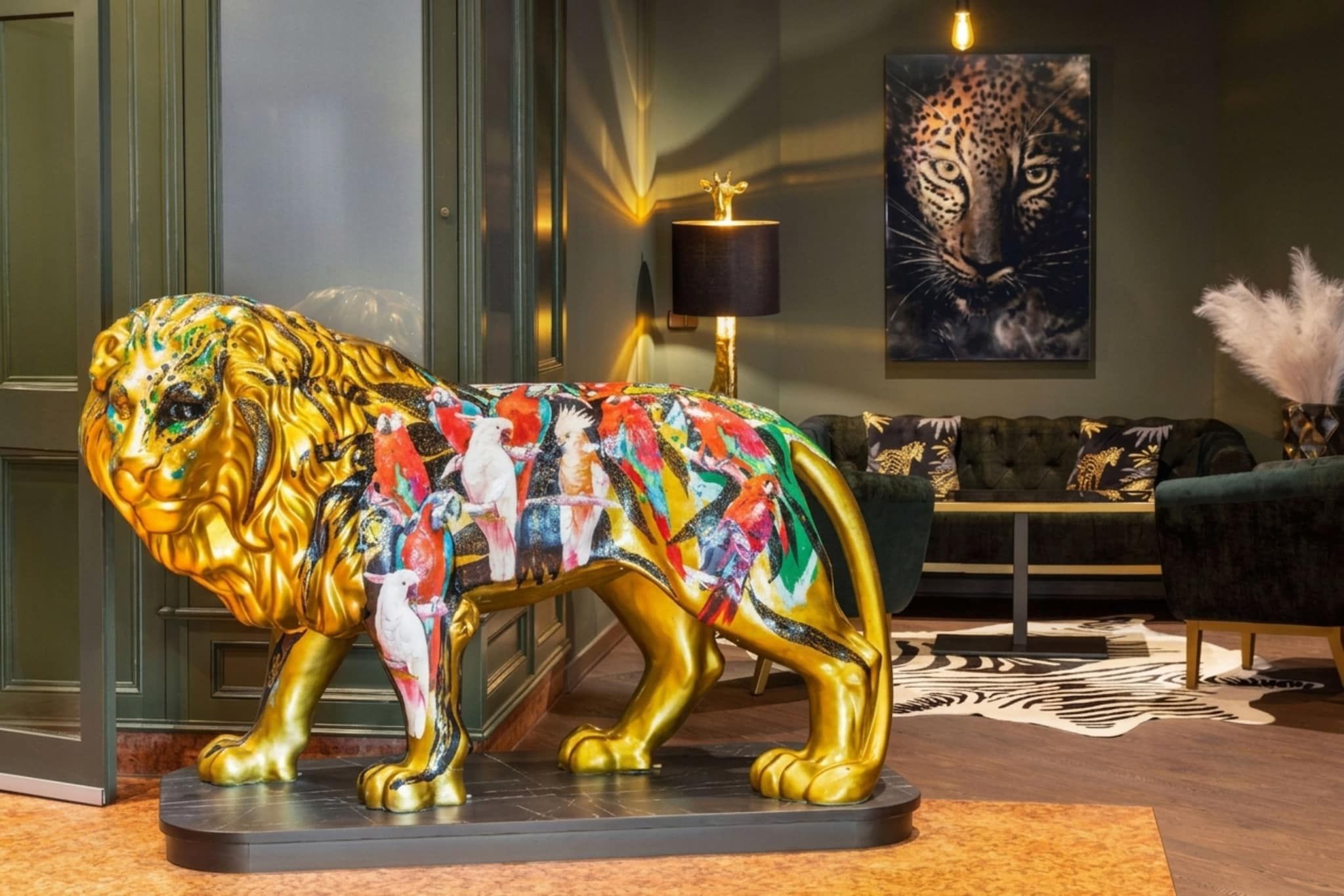 Eine goldene Löwenstatue mit farbenfrohen Mustern, ein Leopardenbild, eine Lampe und ein Sofa in einem Zimmer.